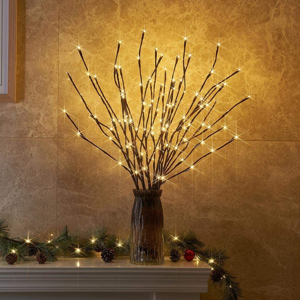 Decorative branches with lights in a vase on a mantelpiece against a warm-toned wall.