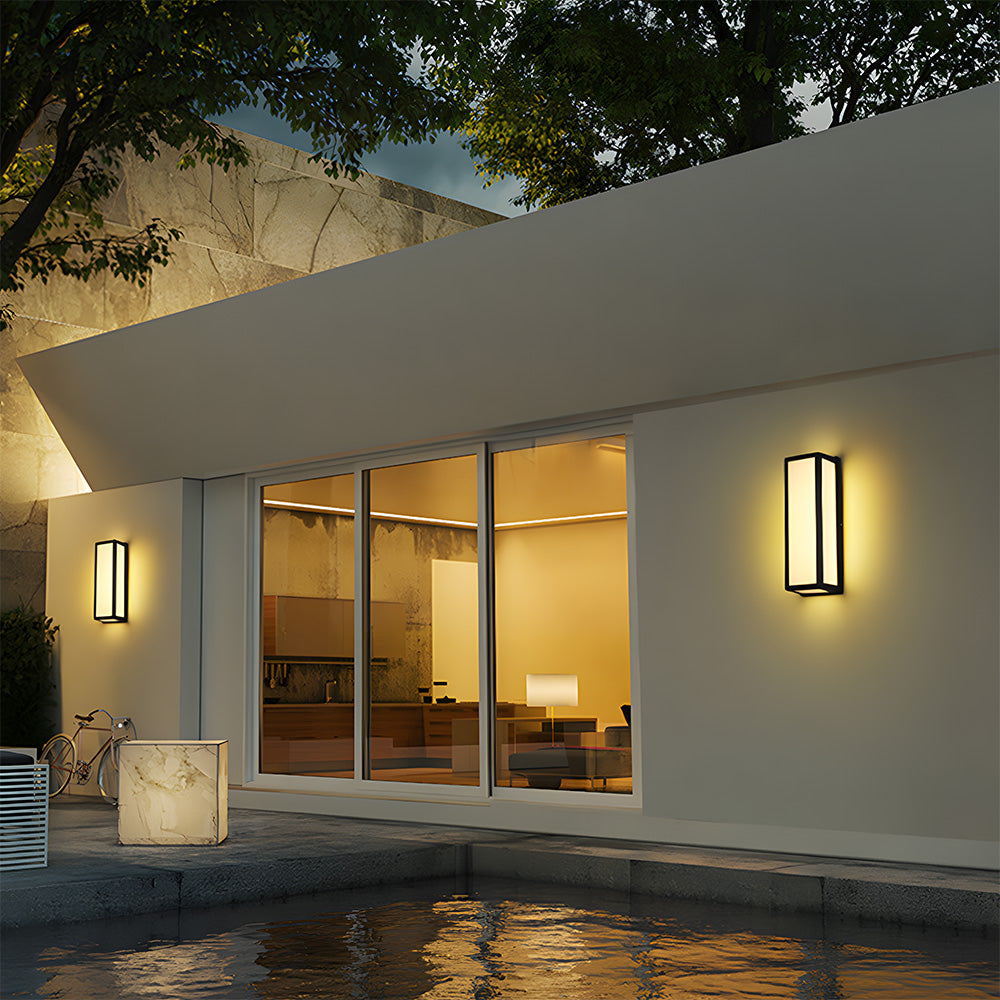Modern house exterior with illuminated interior, wall-mounted lights, and a tree.