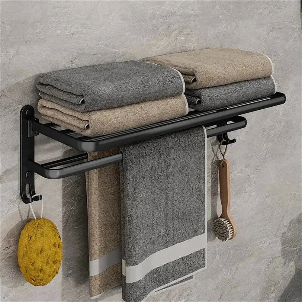 Towel rack with folded towels, a sponge, and a brush against a gray tiled wall.