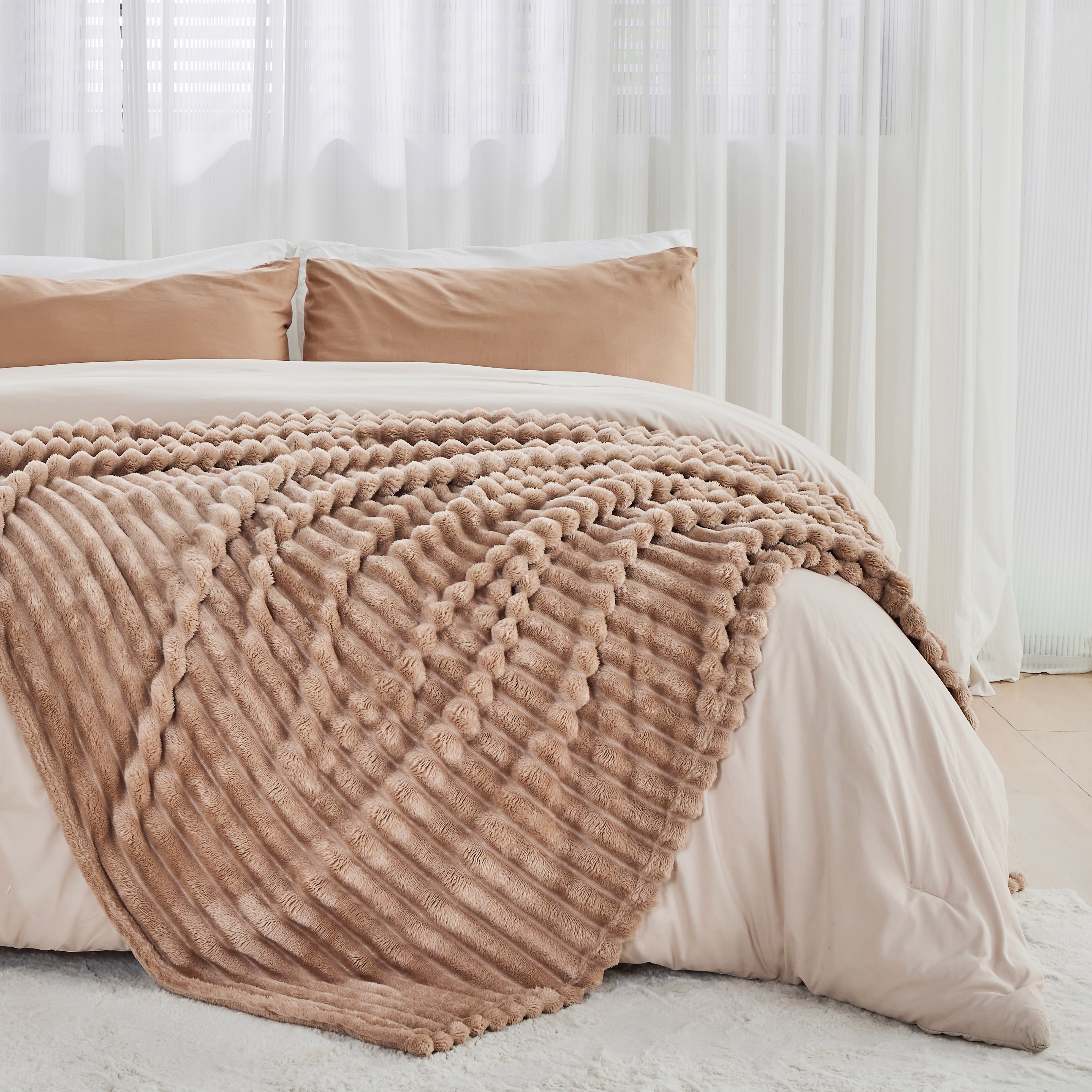 Beige textured blanket draped over a bed with white bedding and pillows.
