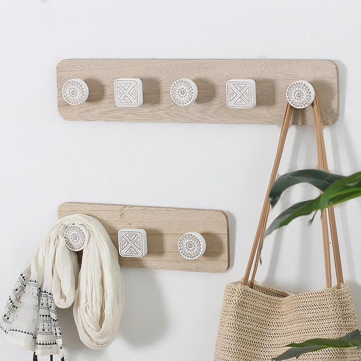 Wooden wall hooks with decorative plates on a white wall, one holding a scarf and the other a bag.