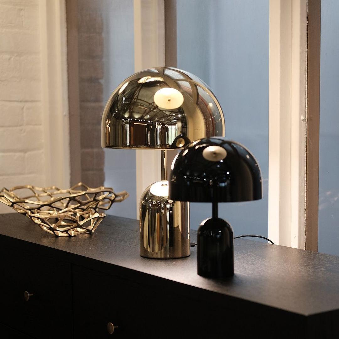 Two table lamps, one gold and one black, on a dark surface with a light blue wall in the background.