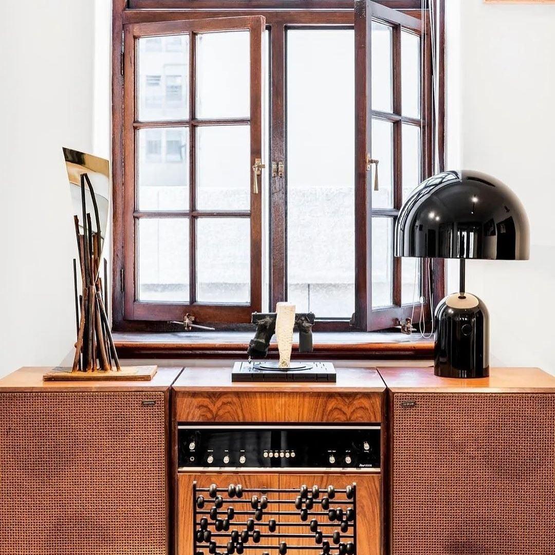 Wooden cabinet with a black lamp and decorative items in front of a window.
