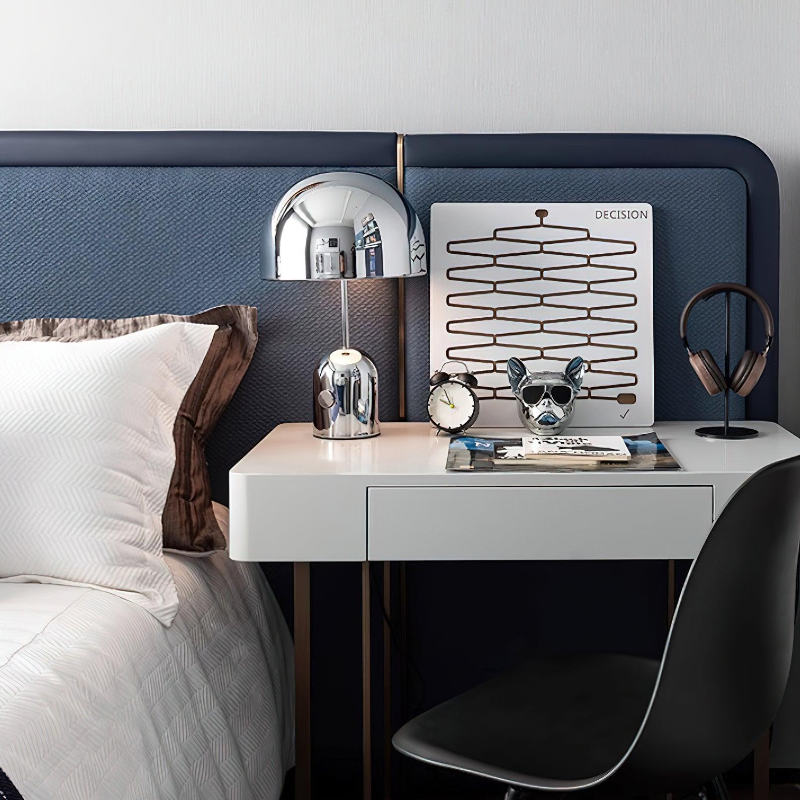 White desk with lamp, clock, and decorative items against a blue headboard.