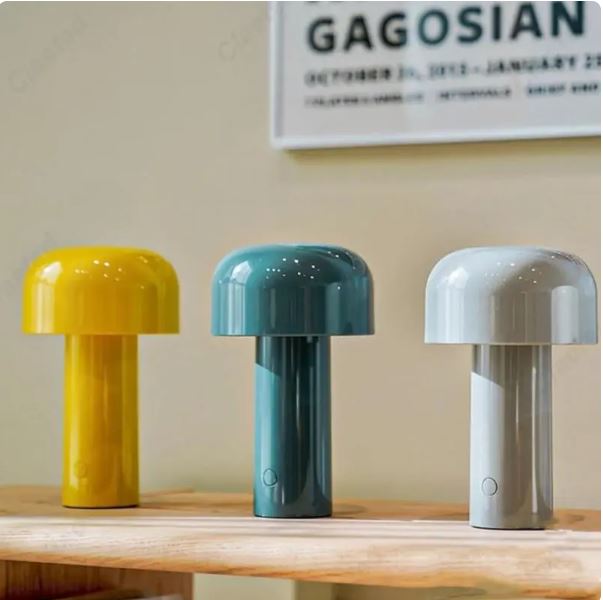 Three colorful table lamps on a wooden surface with a 'Gagosian' poster in the background.
