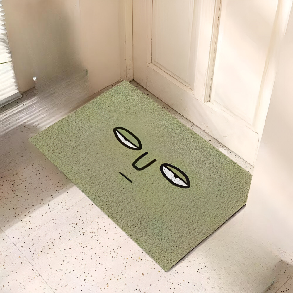 Green doormat with black text and symbols on a light wooden floor.