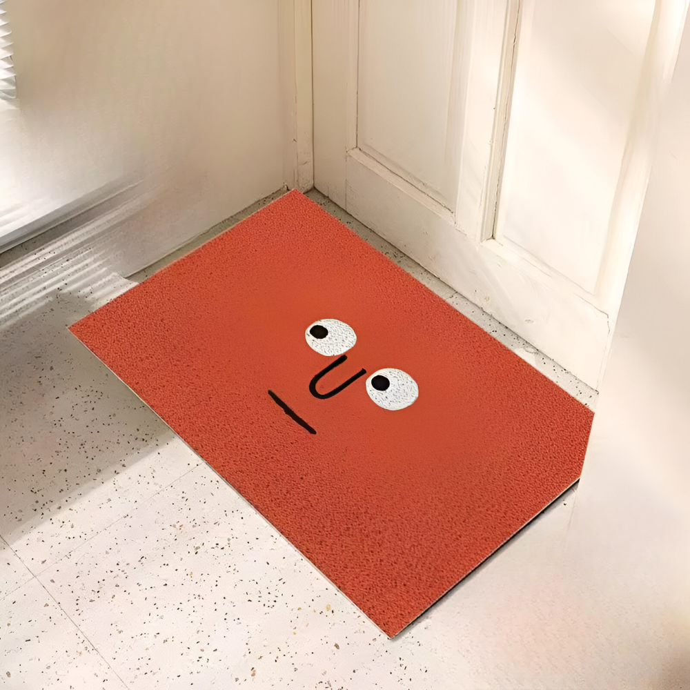 Orange doormat with a face design on a white floor.