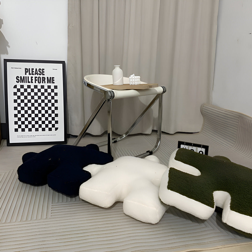 Three plush cushions in black, white, and green on a floor with a small table and decorative items in the background.