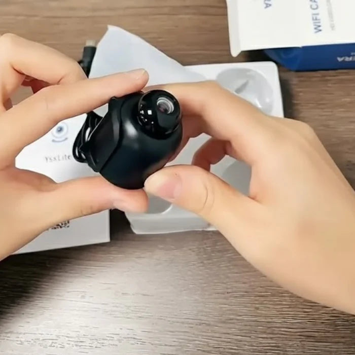 Person holding a small black camera on a wooden surface with a blurred background