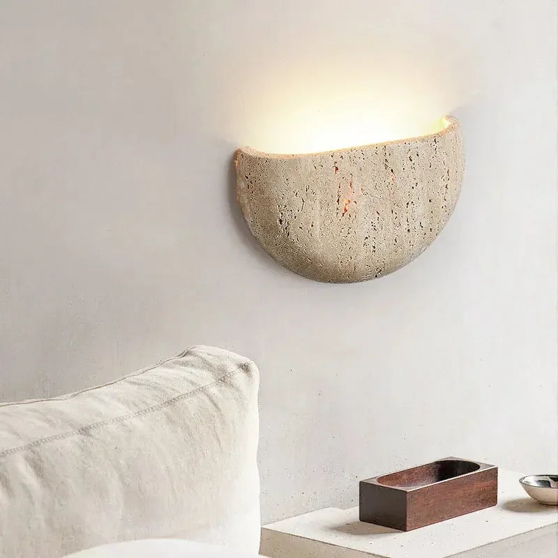 Cement wall sconce on a neutral wall with a pillow and small wooden box in the foreground.