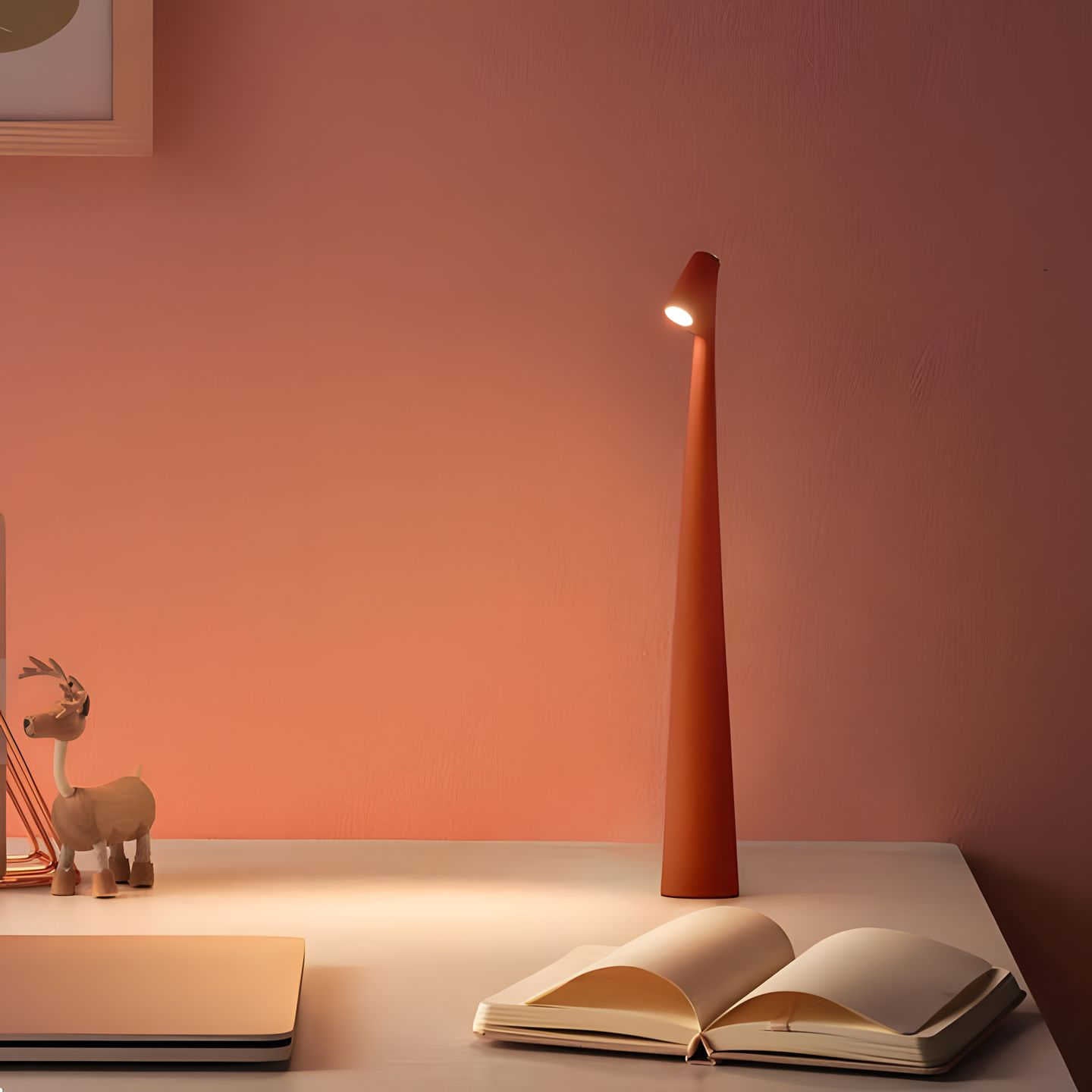 Orange floor lamp on a white surface with an open book and small deer figurine against a pink wall.