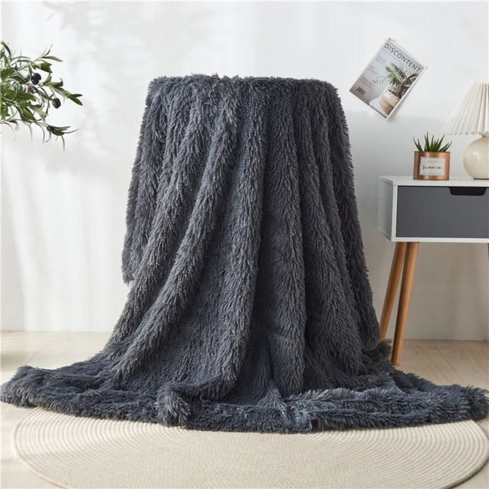Gray fluffy blanket draped over a chair in a room with a plant and small table in the background.