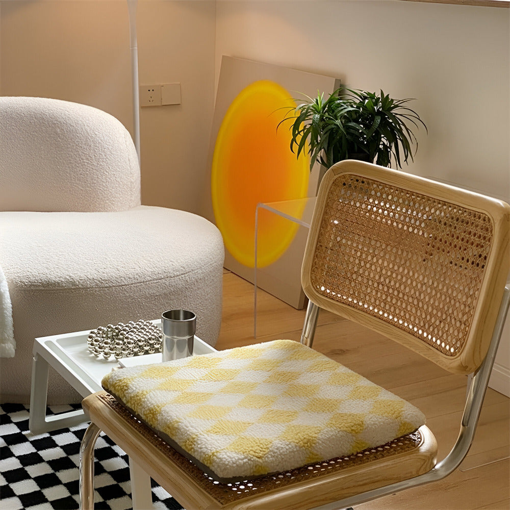 Chair with a yellow and white checkered cushion in a room with a plant and abstract art.