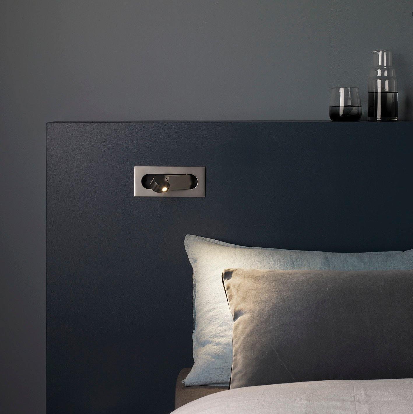 Dark headboard with built-in light fixture and decorative items on a gray wall.
