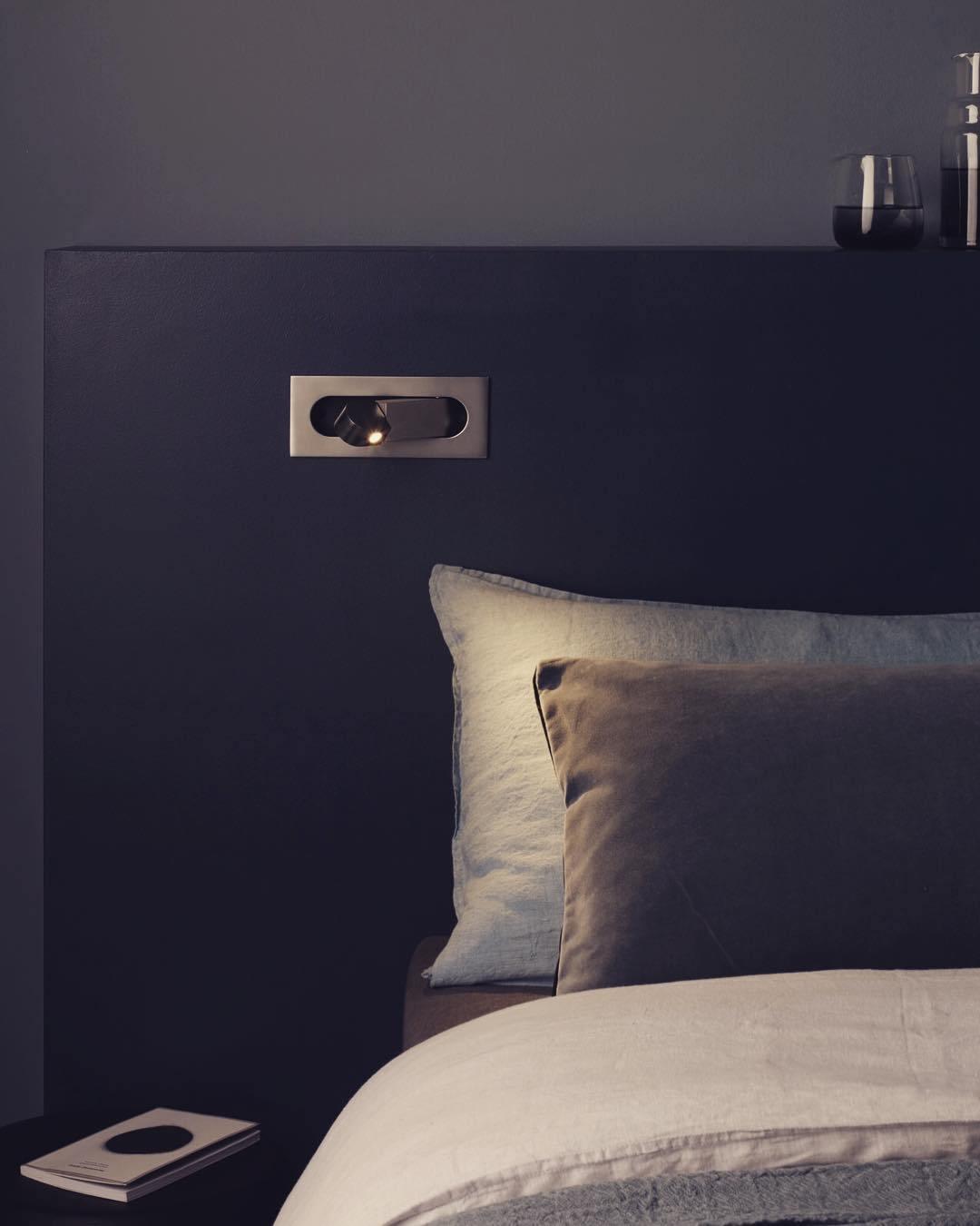Dark headboard with built-in light fixture above a bed with pillows.