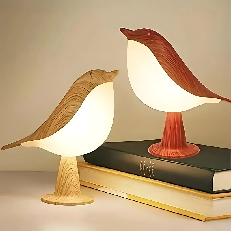 Two bird-shaped lamps on top of books with a warm glow.