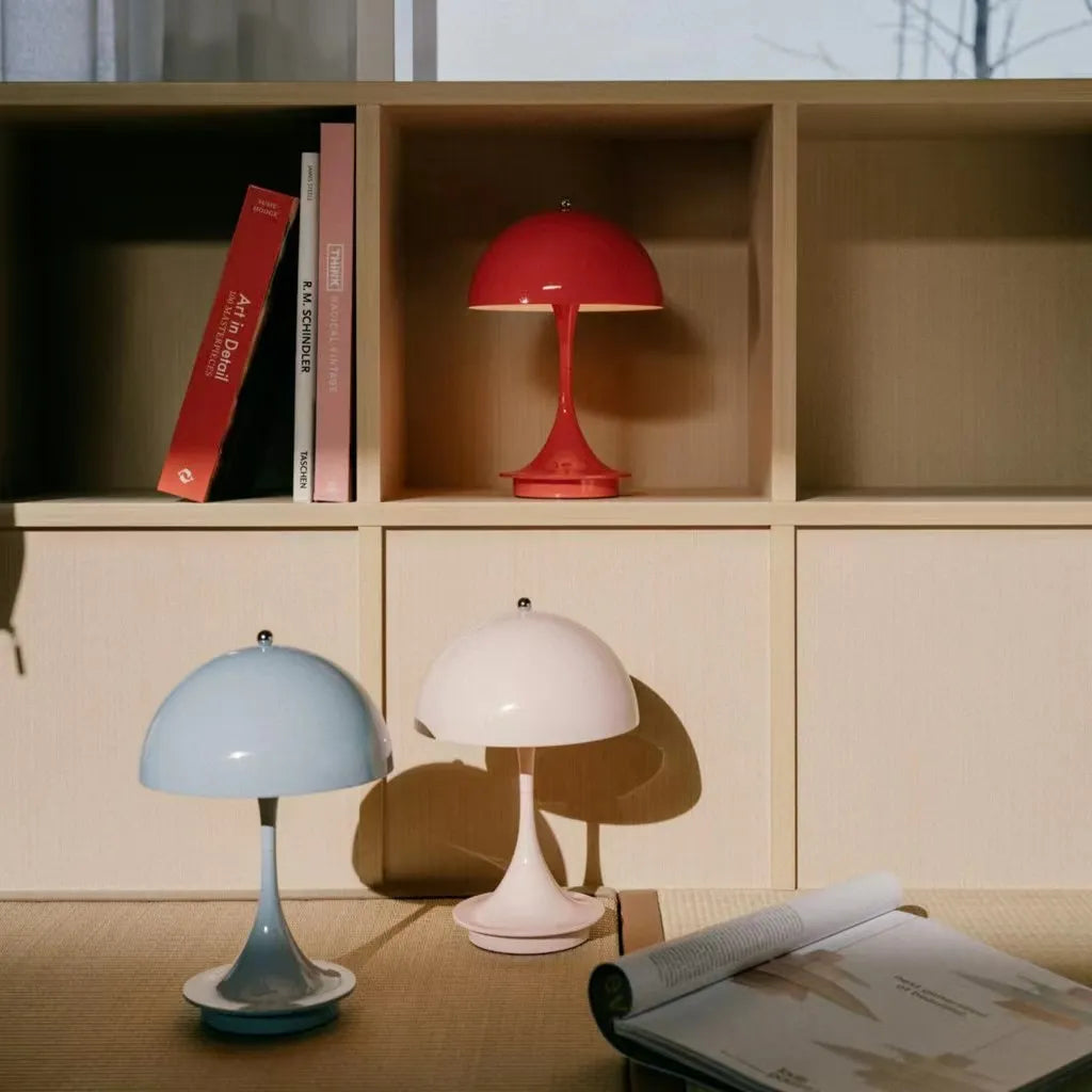 Three small table lamps in blue, white, and red on a wooden shelf with books.