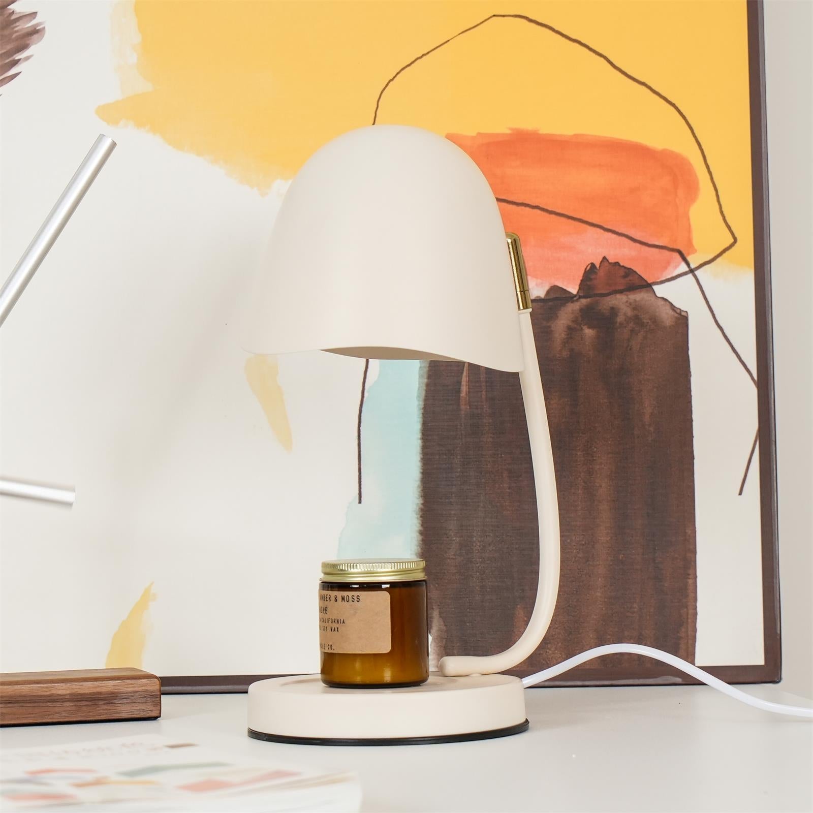 White lamp with a small jar on a surface in front of abstract art
