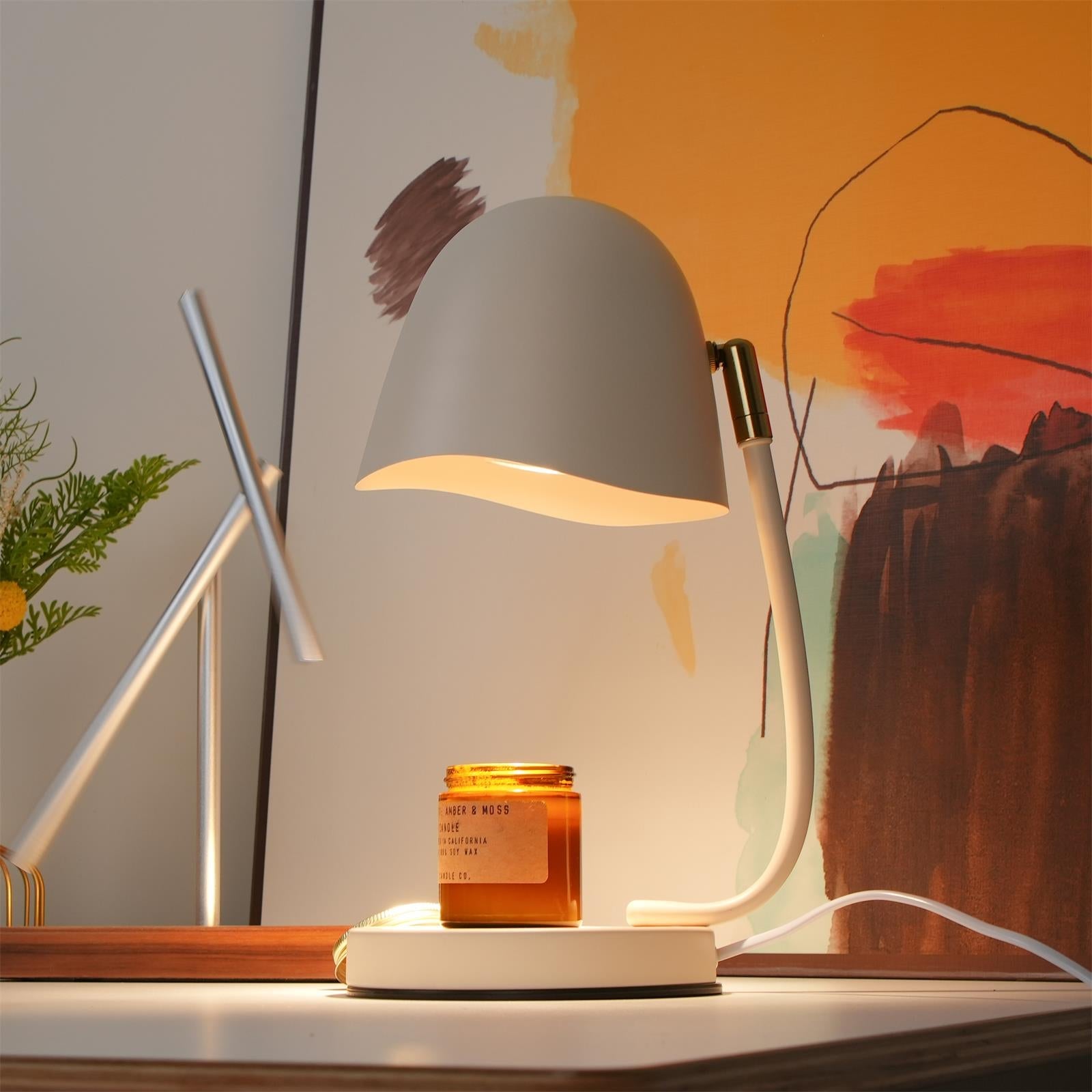 Table lamp with a jar of candle on a desk in front of a colorful abstract painting