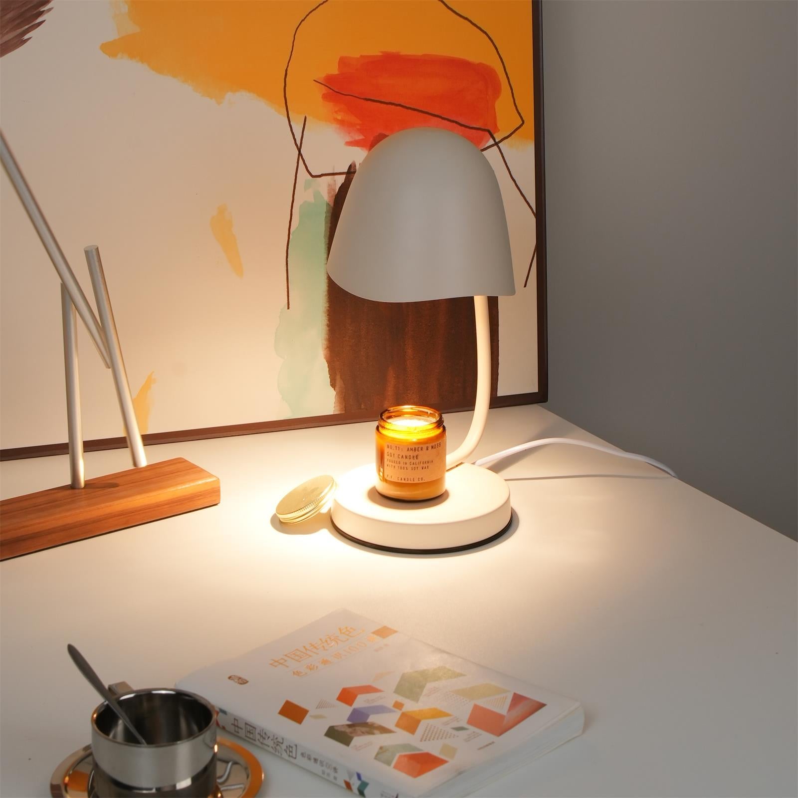 Table lamp with a lit candle on a table next to a book and small pot.