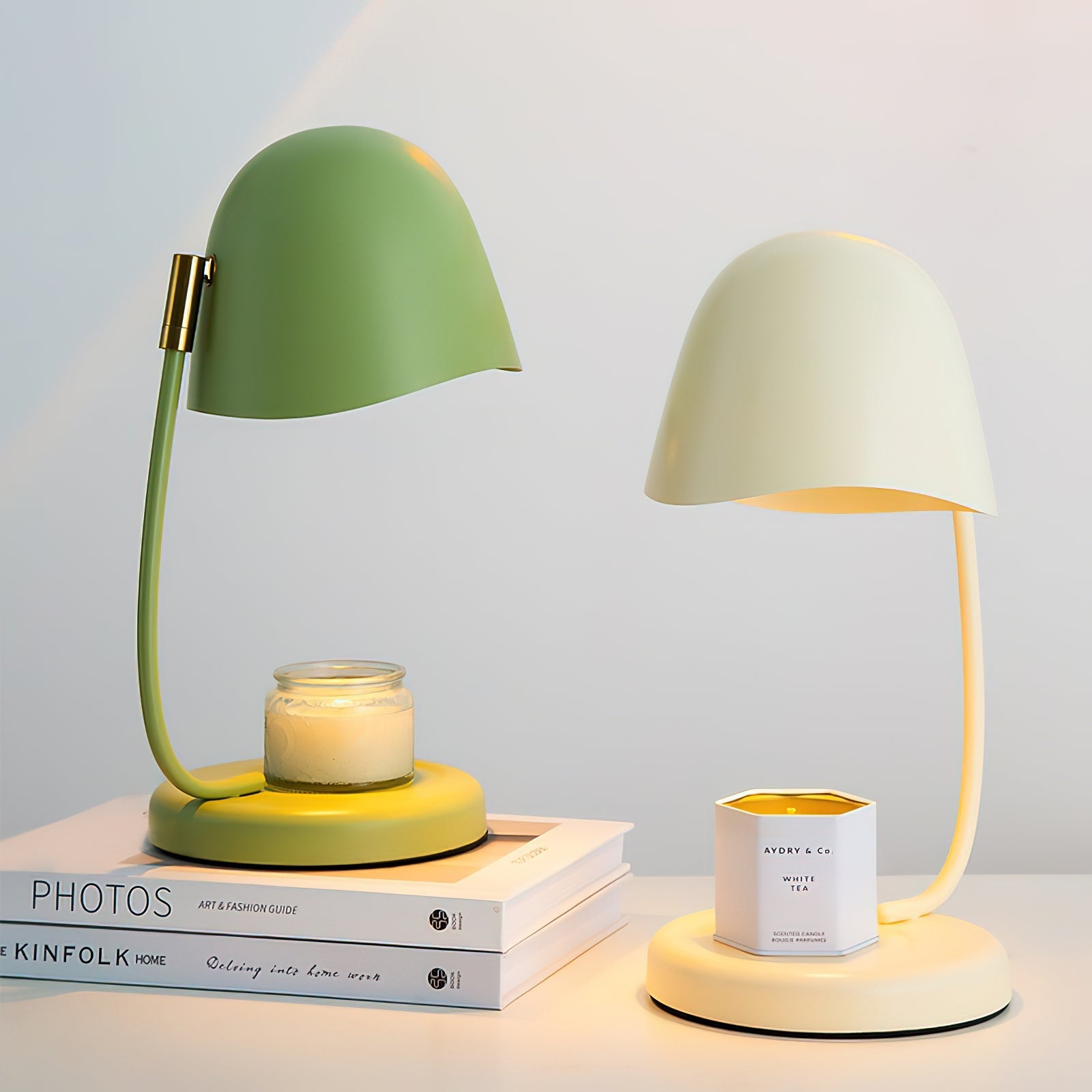 Two table lamps, one green and one white, on a surface with books and a candle.