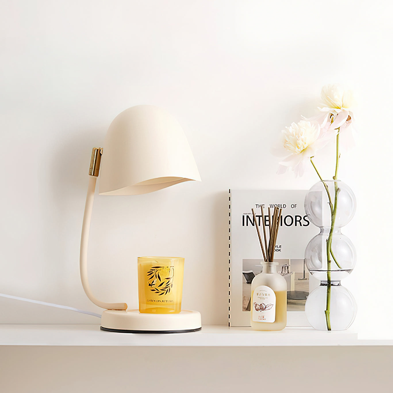 Decorative setup with a lamp, candle, diffuser, and book on a shelf.