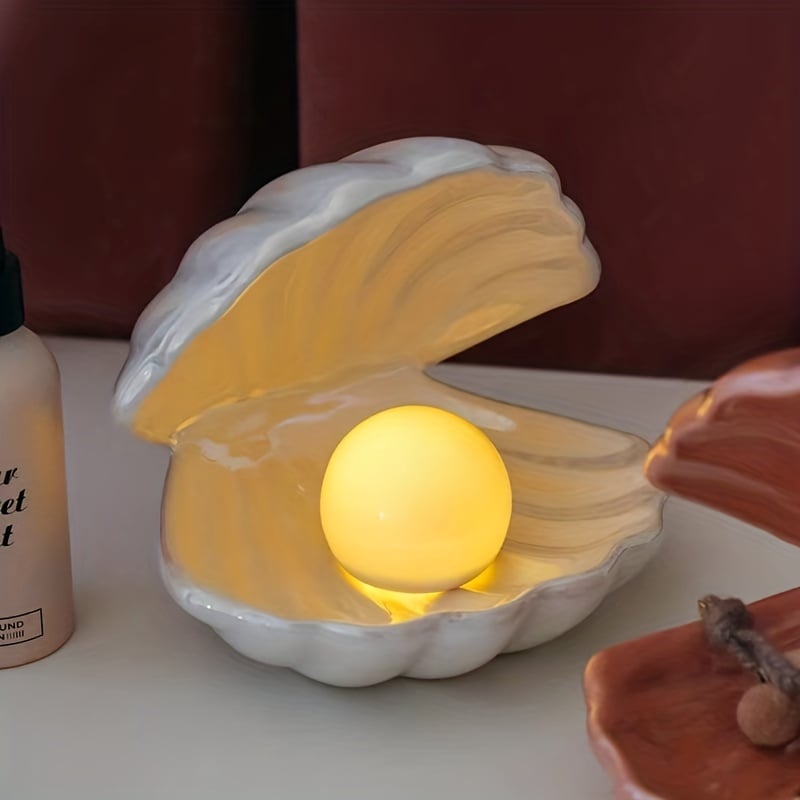 Shell-shaped night light with a glowing pearl inside on a table.