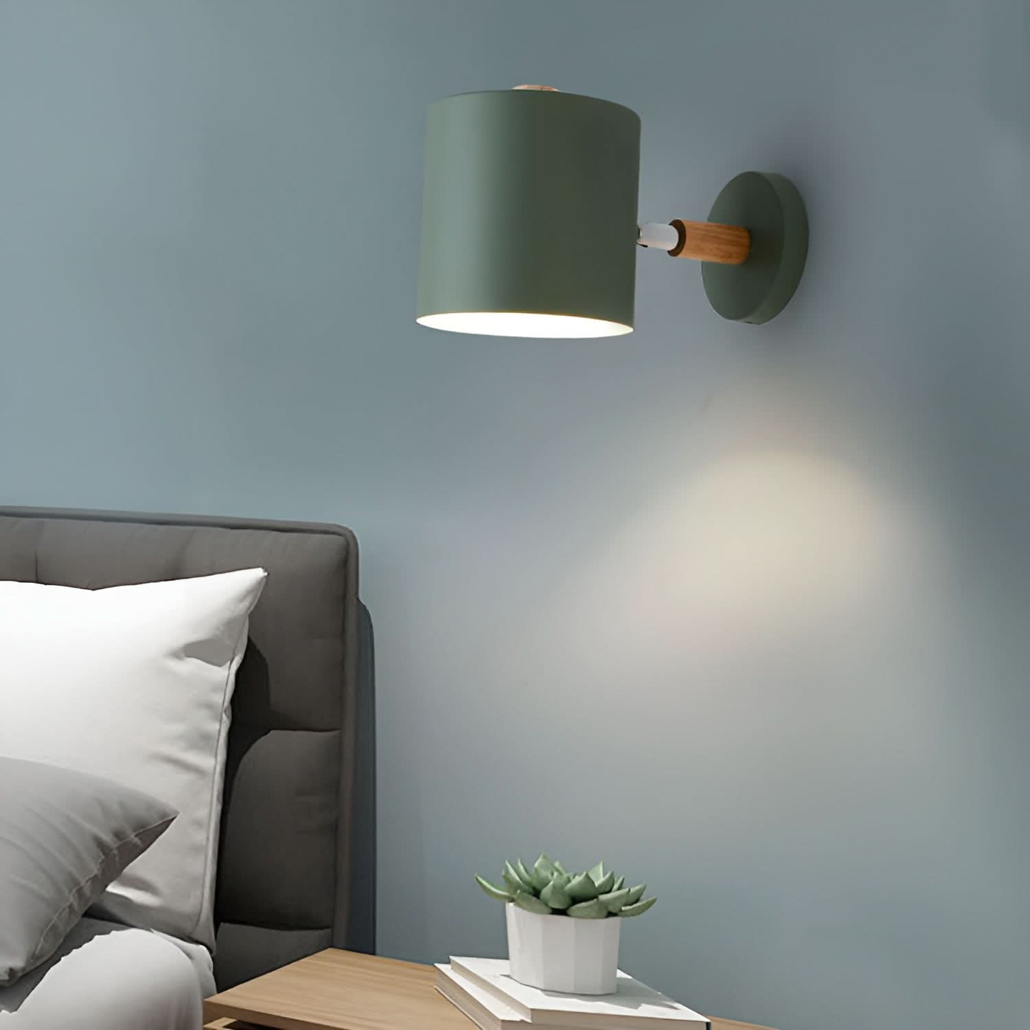 Green wall lamp on a gray wall above a bed with pillows and a small plant.