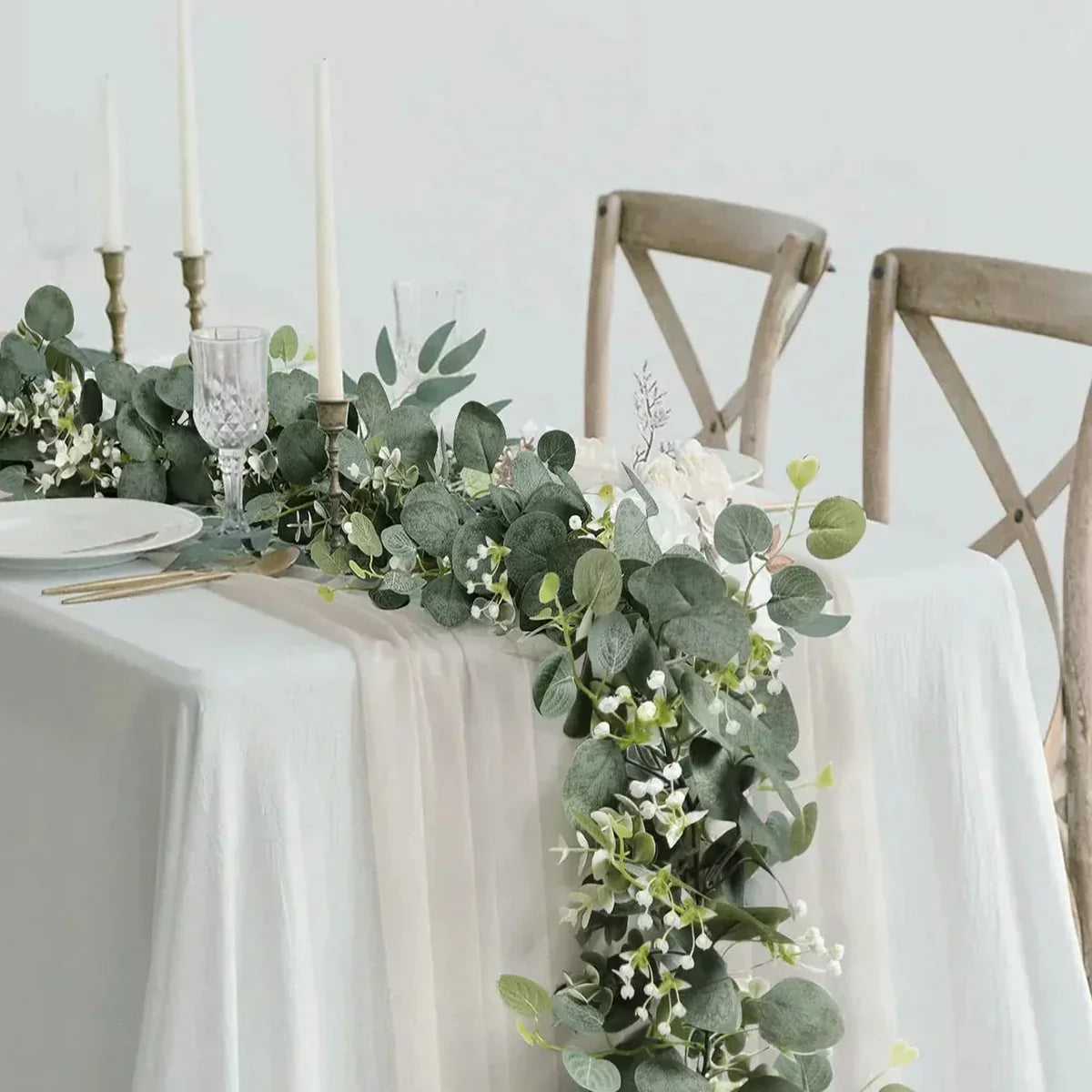 Decorative table setting with greenery and candles on a white tablecloth.