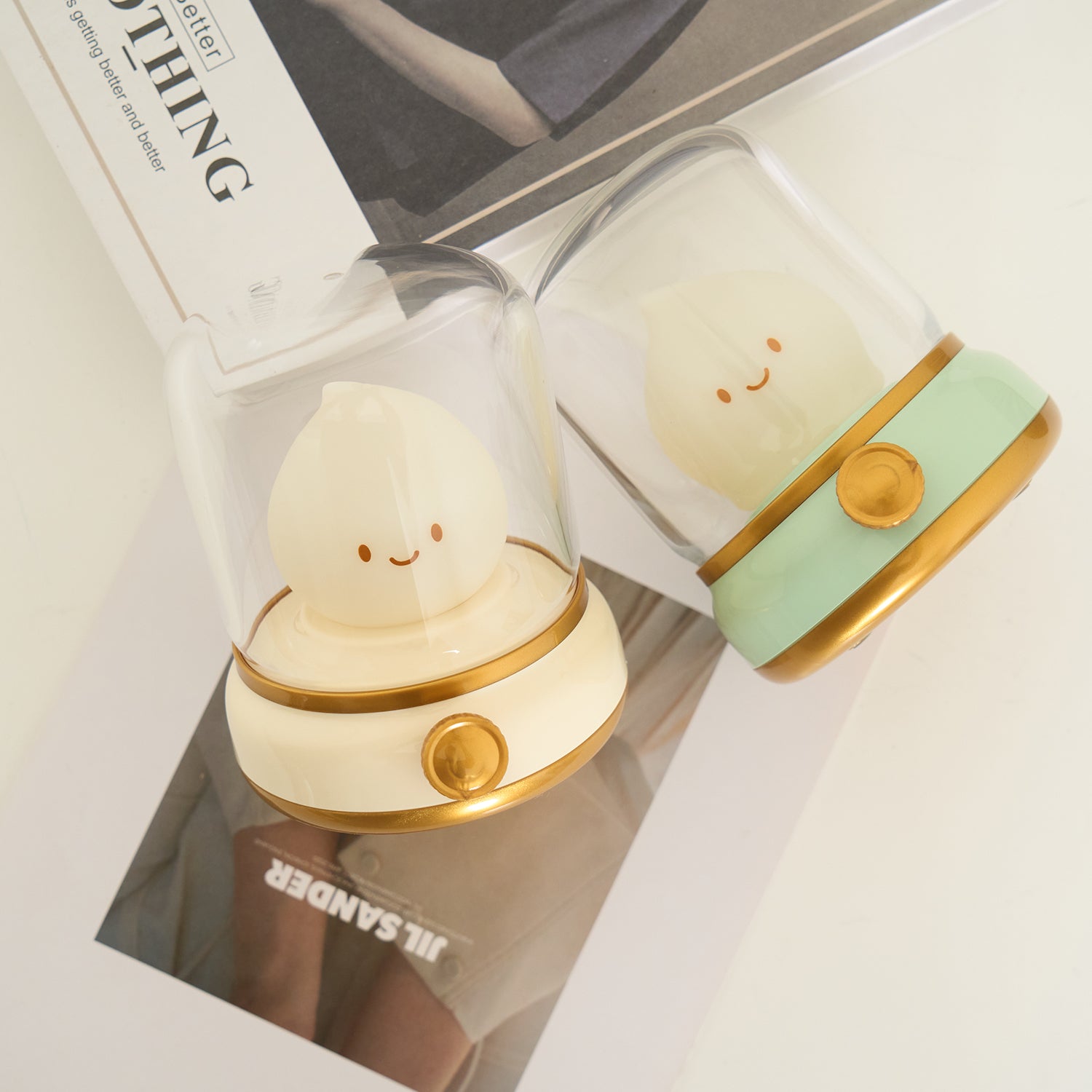 Two cute lamp-shaped night lights with smiling faces in a box, one gold and one green.