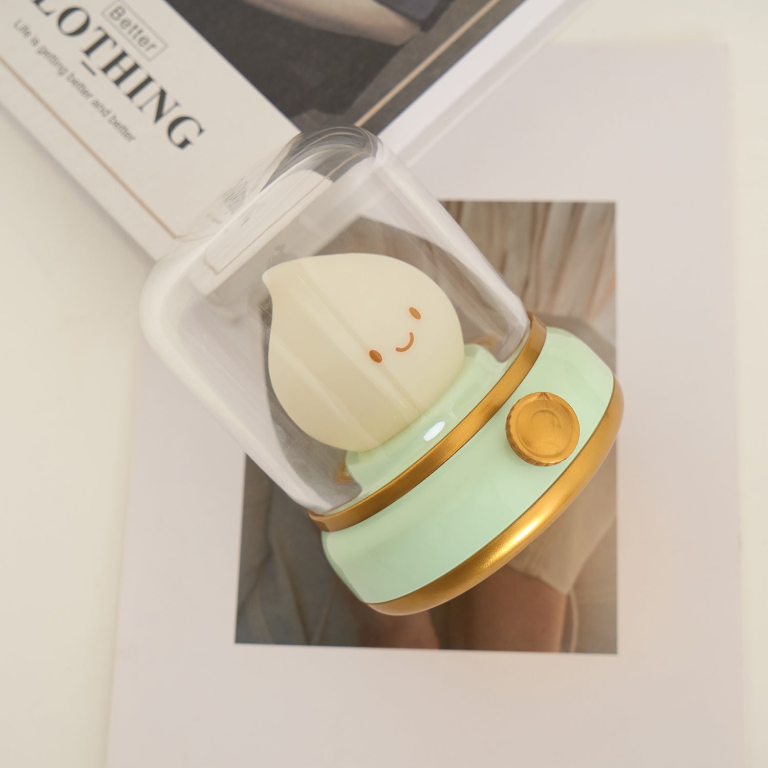 Small plush toy resembling a character in a green outfit with gold helmet inside a clear plastic box.