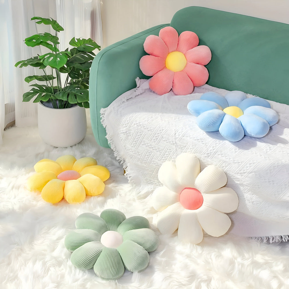 Flower-shaped cushions in various colors on a white surface with a plant in the background.