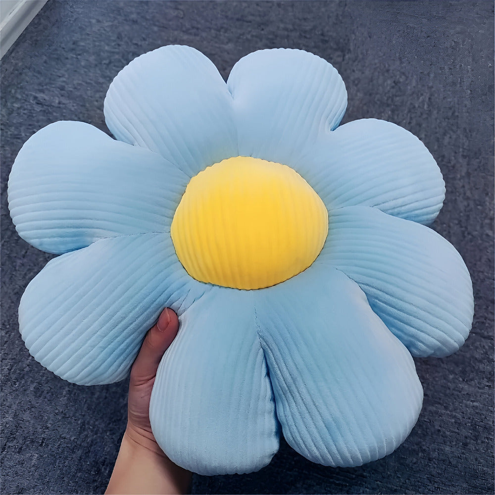 Blue flower-shaped pillow with a yellow center held by a hand on a dark surface