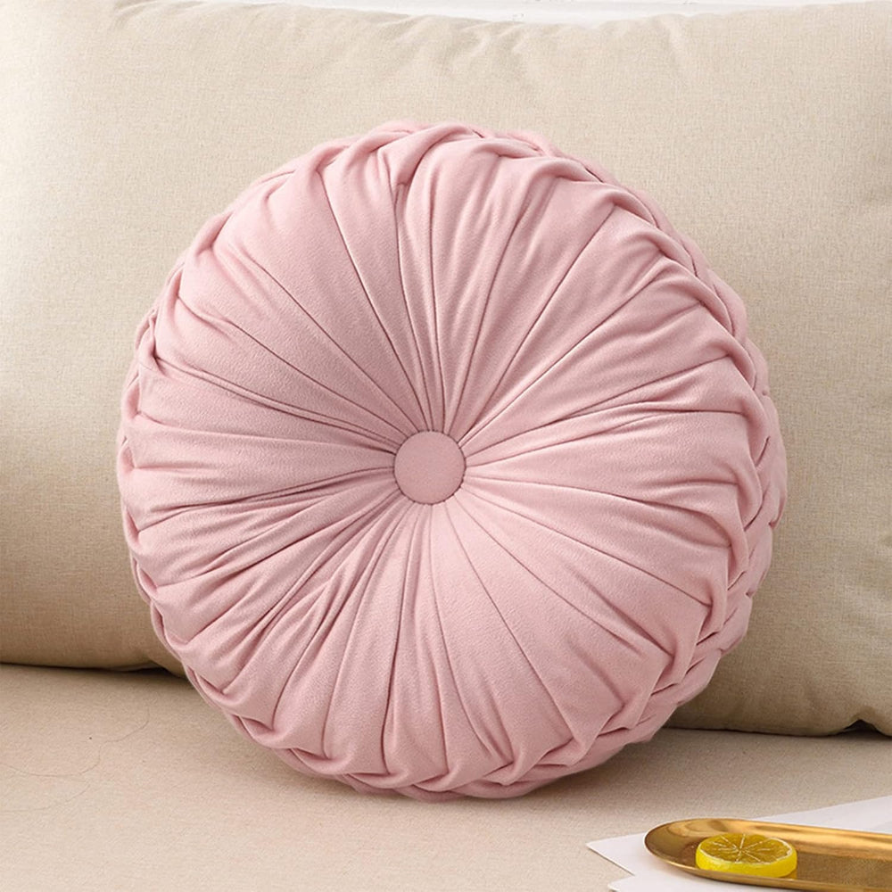 Pink round pillow on a beige sofa with a lemon and wooden spoon on a table.
