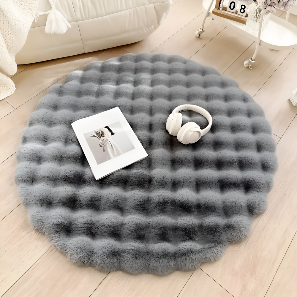 Round gray fluffy rug on a wooden floor with a book and headphones on top