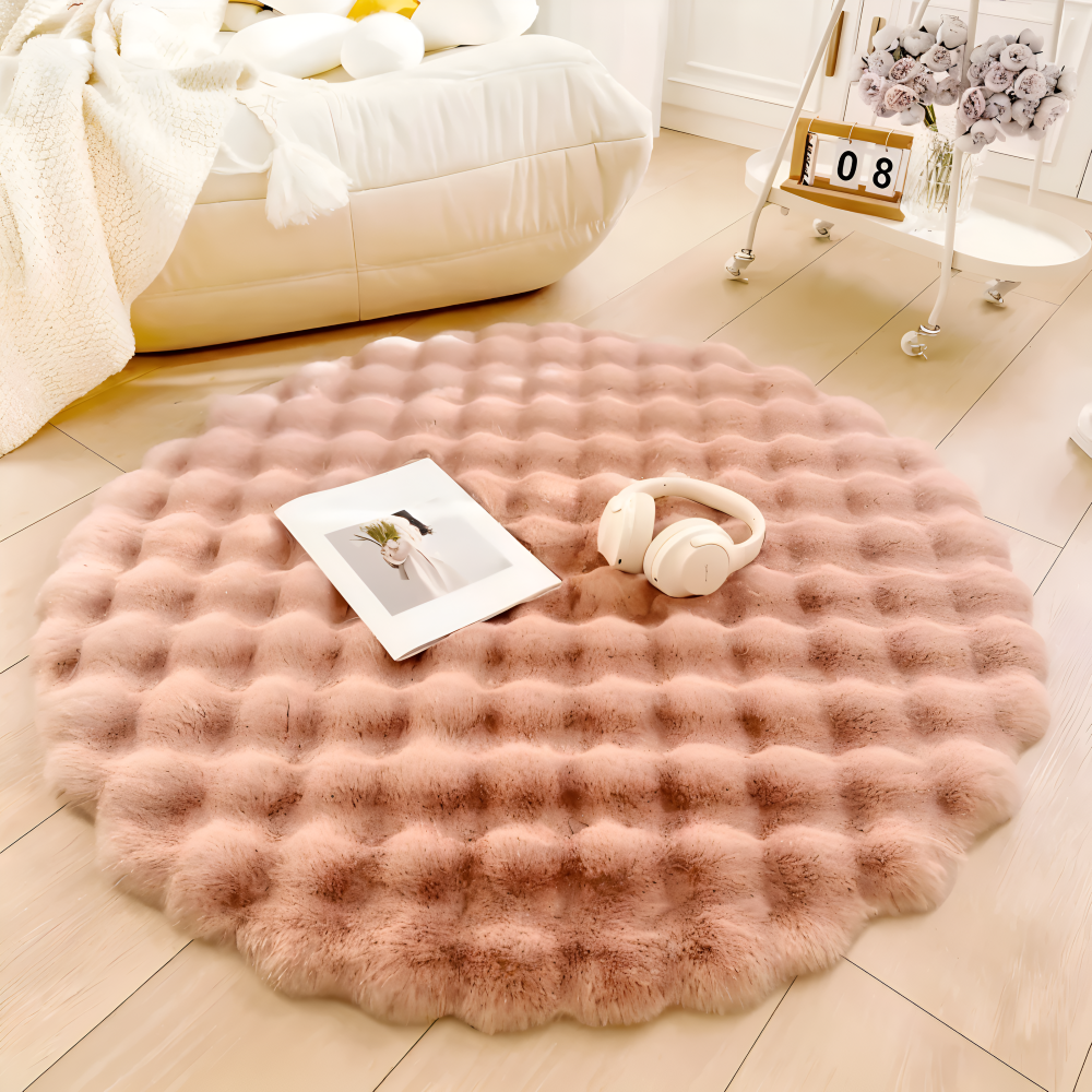Round pink rug on a wooden floor with a book and headphones on top, in a cozy living room setting.