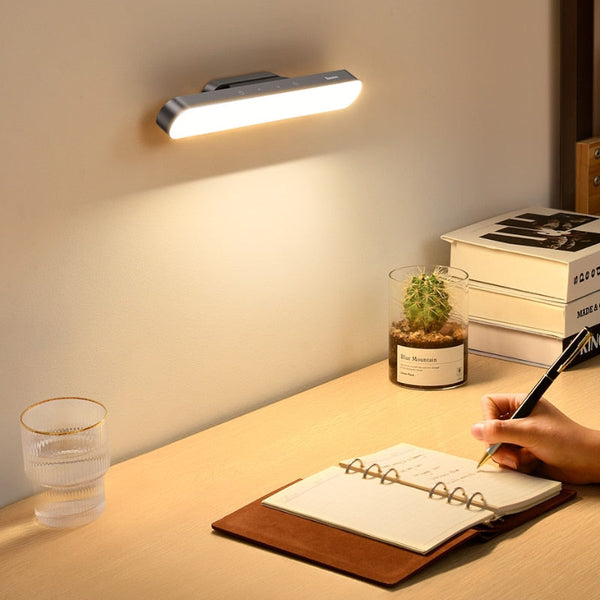 Desk setup with a wall-mounted light, notebook, pen, and small plant.