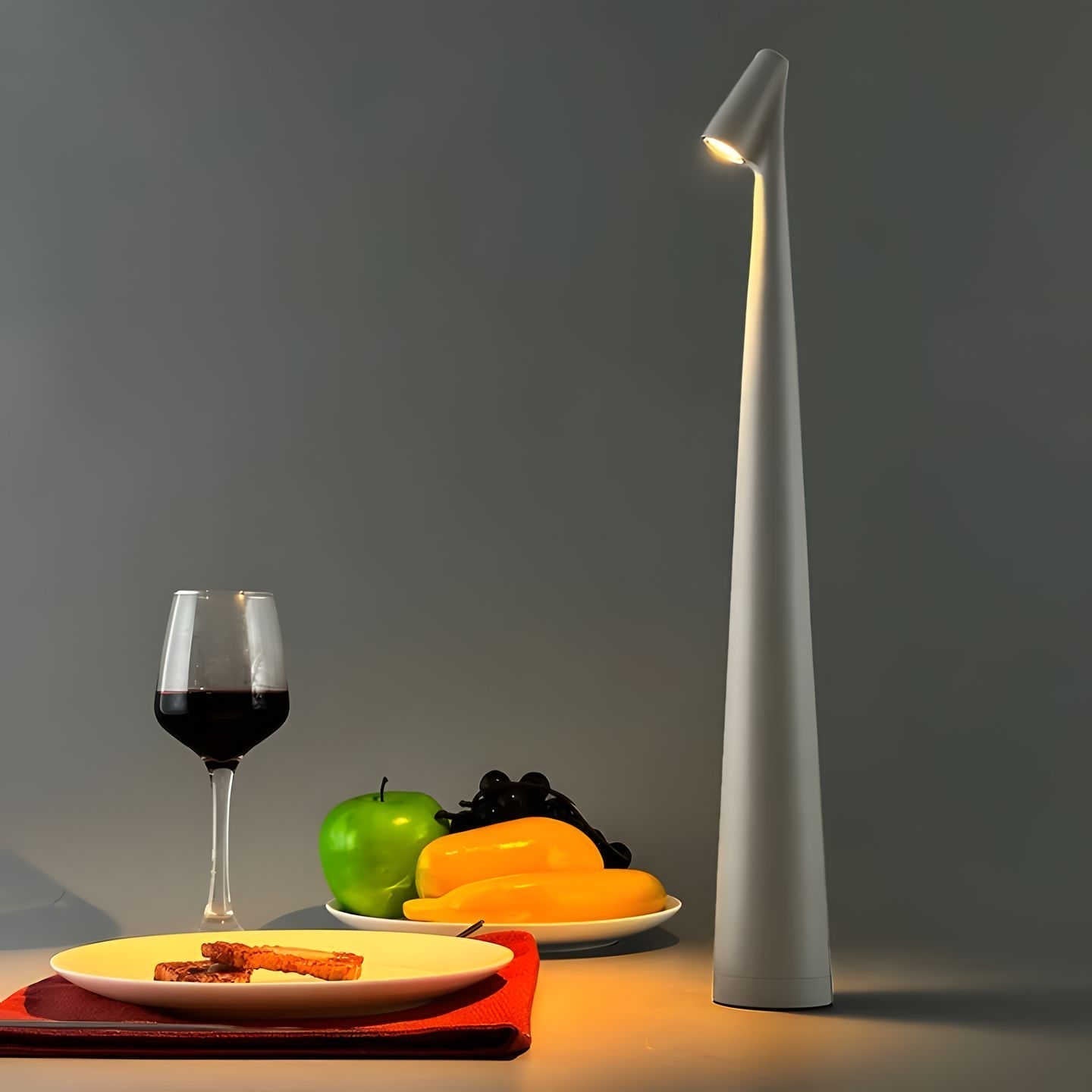 Modern table lamp on a table with a glass of red wine, apples, and a plate of food.