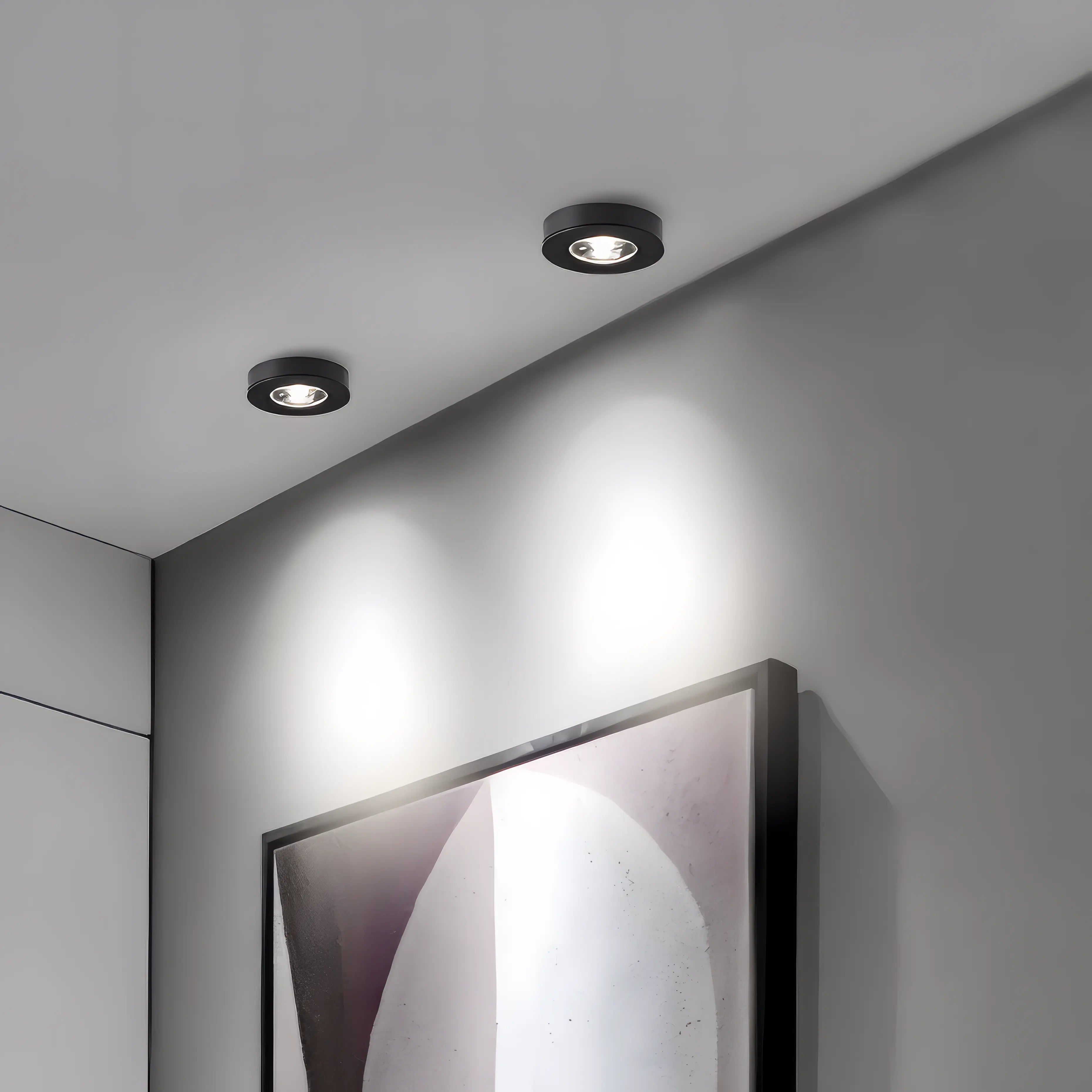 Two recessed ceiling lights on a gray wall with a framed abstract painting.