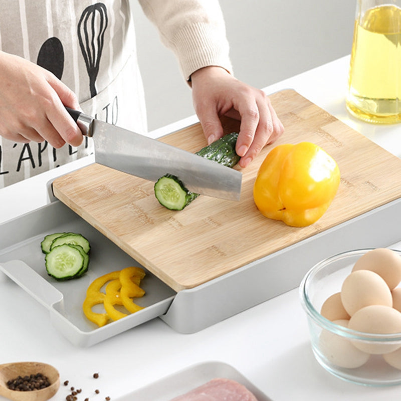 Person cutting vegetables on a wooden cutting board with a knife, surrounded by kitchen items.