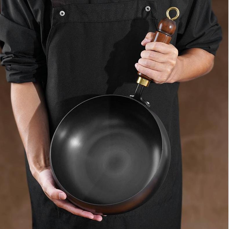 Person holding a black frying pan with a wooden handle against a brown background