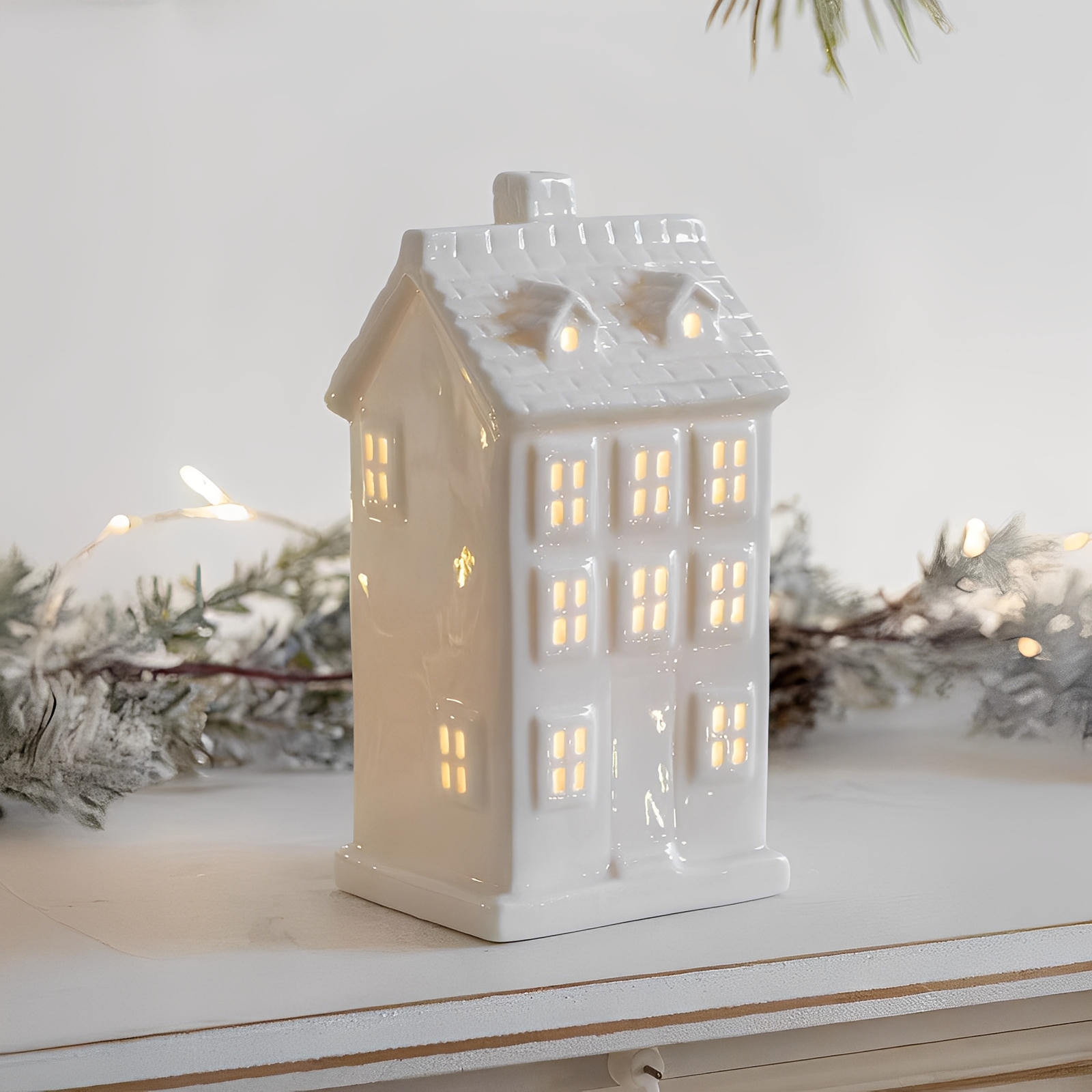 White ceramic house-shaped lantern with glowing interior on a white surface with decorative elements.