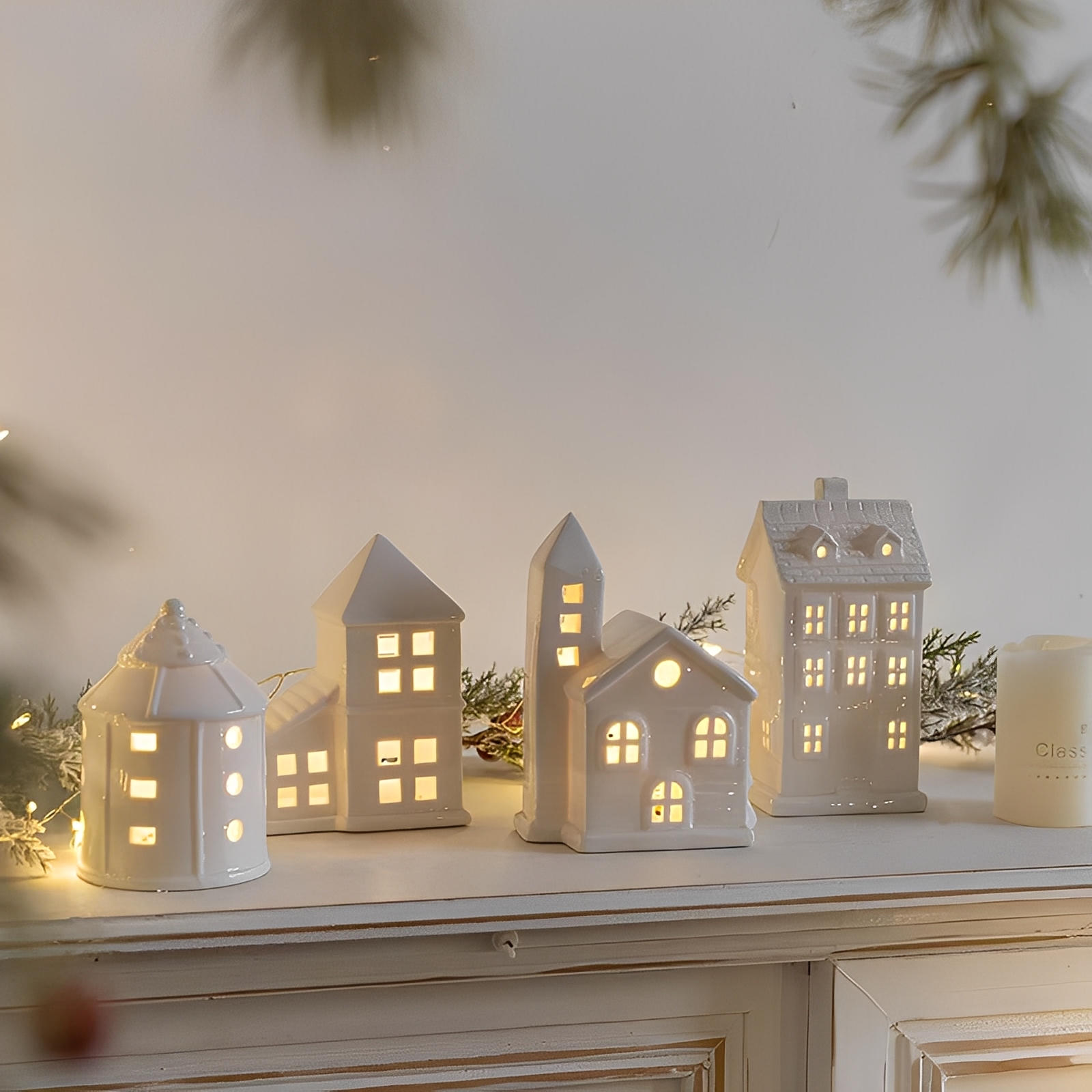 Set of white ceramic houses with lit windows on a mantelpiece.