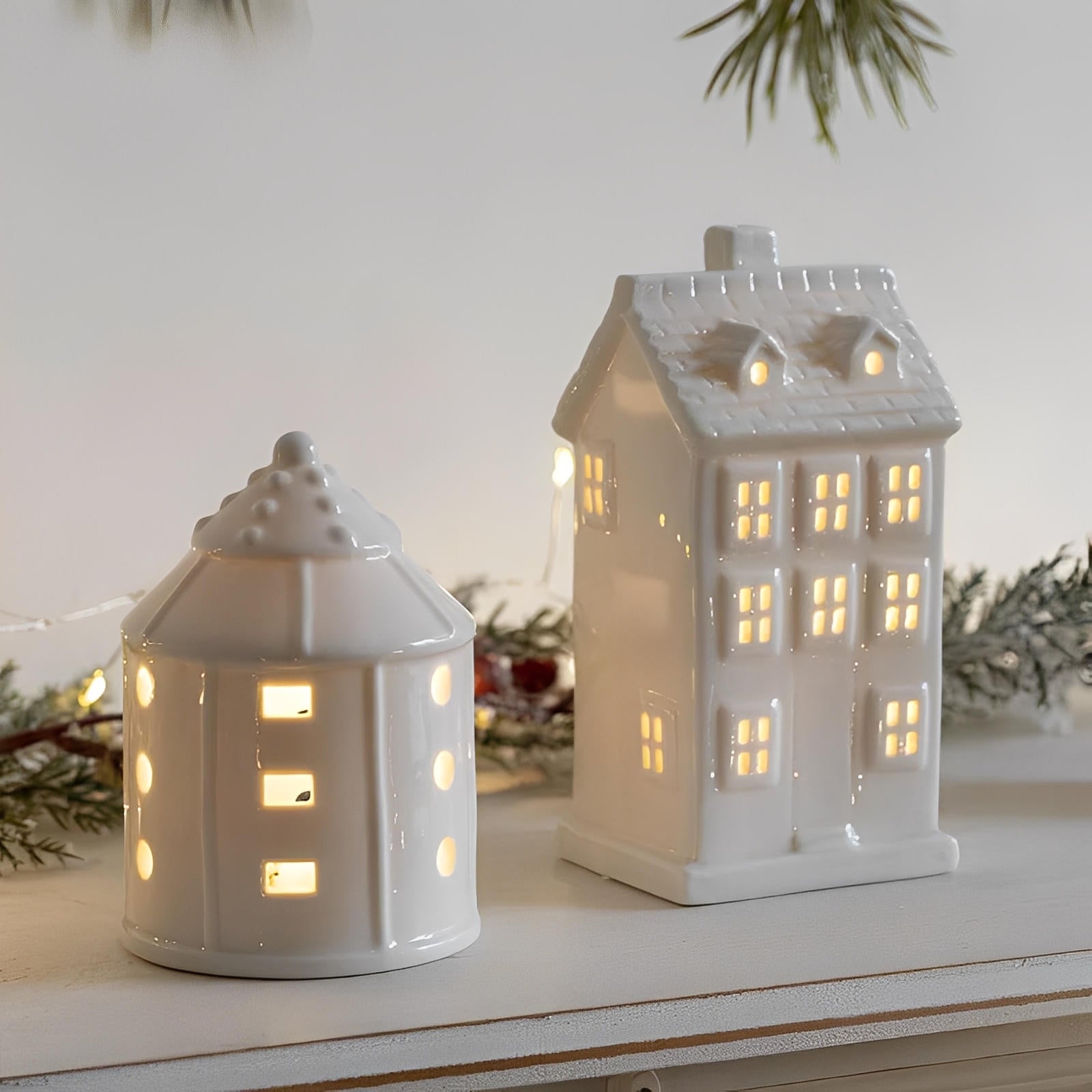 Two white ceramic house-shaped lanterns with lit interiors on a wooden surface.