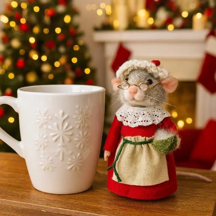 White mug with snowflake design next to a decorative mouse figurine in a festive setting with a Christmas tree and stockings.