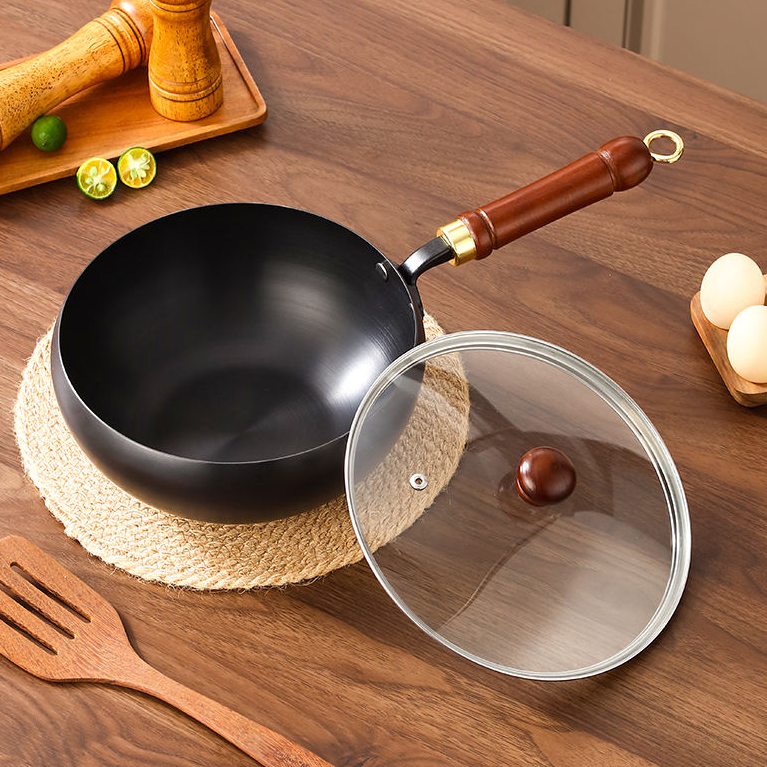Black wok with wooden handle on a wooden table with a glass lid