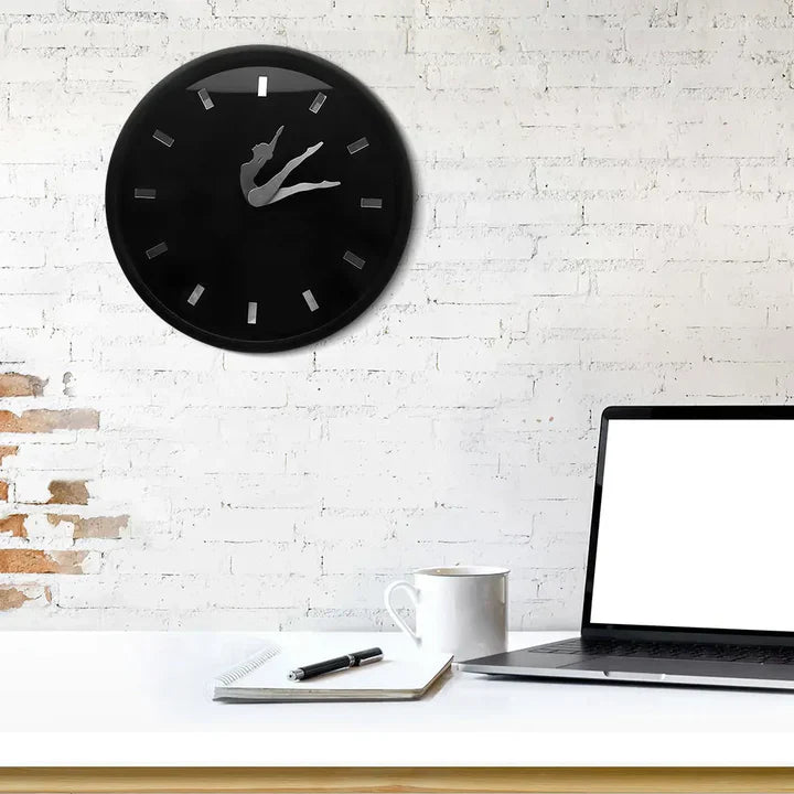 Black wall clock on a white brick wall above a desk with a laptop, mug, and notebook.