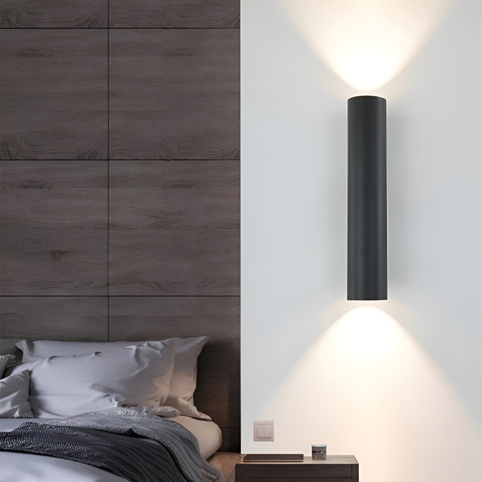 Modern wall-mounted light fixture on a bedroom wall with wooden headboard and bed.