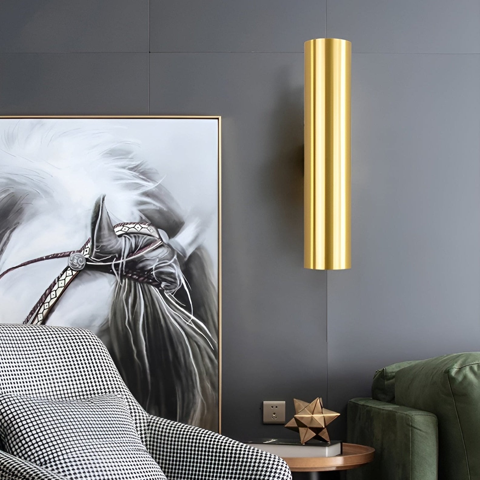 Gold cylindrical wall sconce on a gray wall with a horse painting and green sofa.