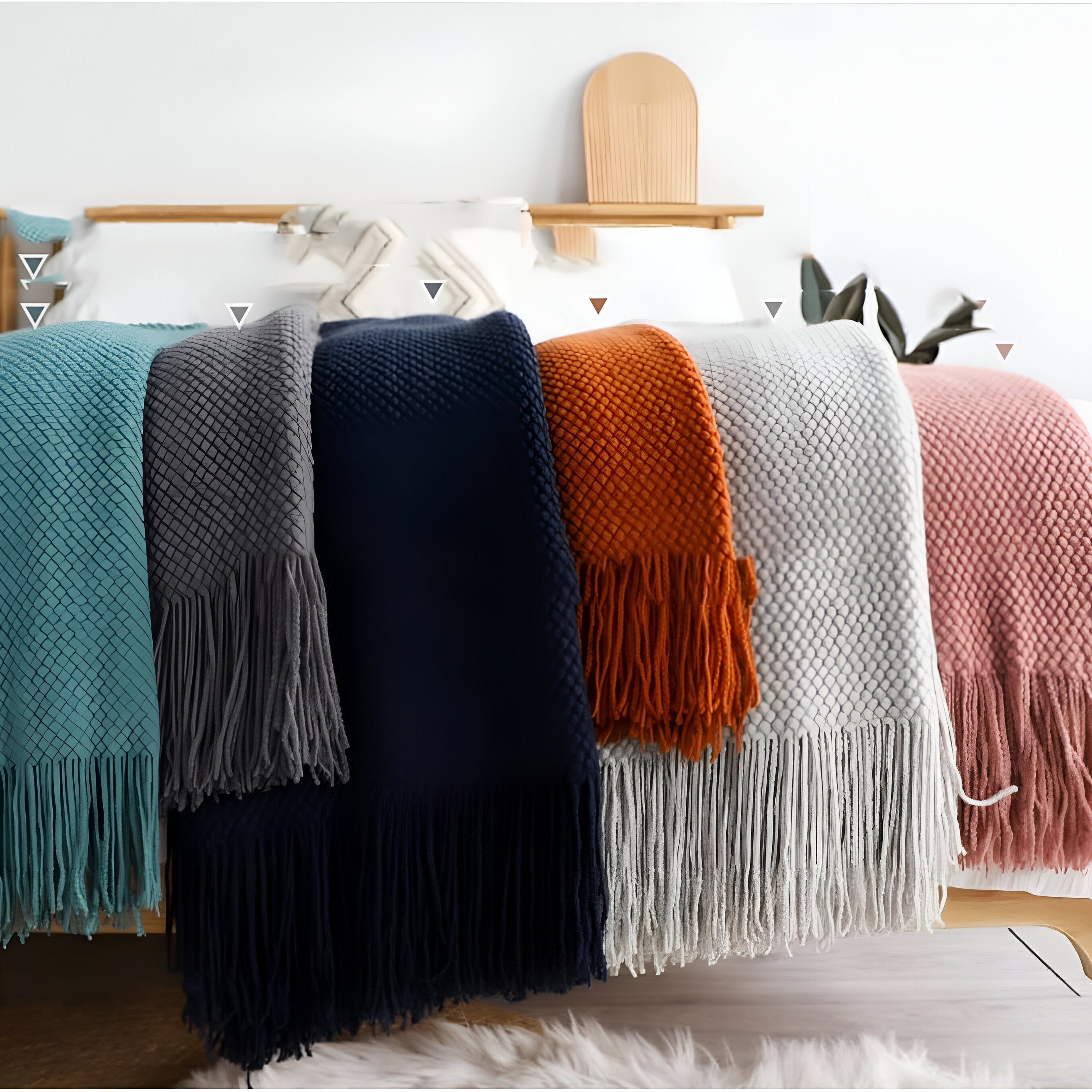 Collection of colorful knitted blankets draped over a bed with a wooden headboard.